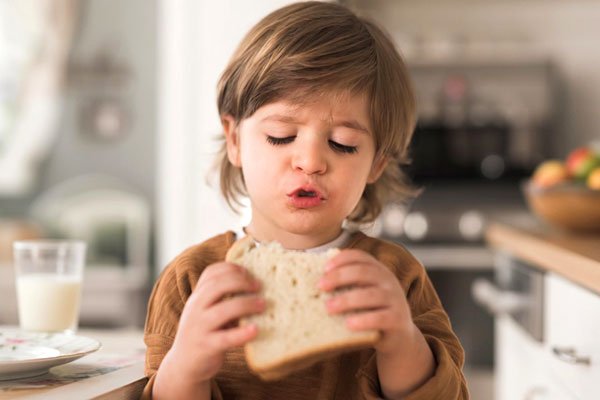 Menino comendo pão de forma sozinho, desenvolvendo coordenação e autonomia alimentar